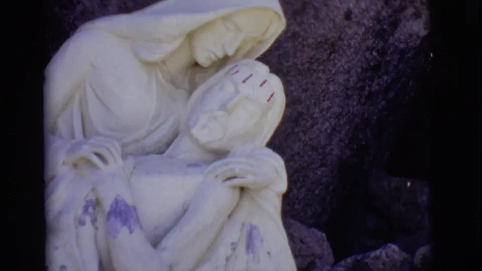 Front-facing 1965 San Luis, Colorado 8mm frame of the marble Virgin Mary cradling Jesus, with weathering visible near the lower figure.