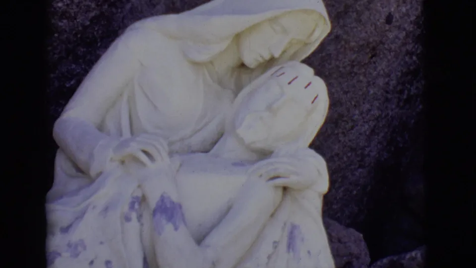 San Luis, Colorado 1965 frame showing the Pieta sculpture centered more fully, with Mary, Jesus, purple staining, and dark rock visible.