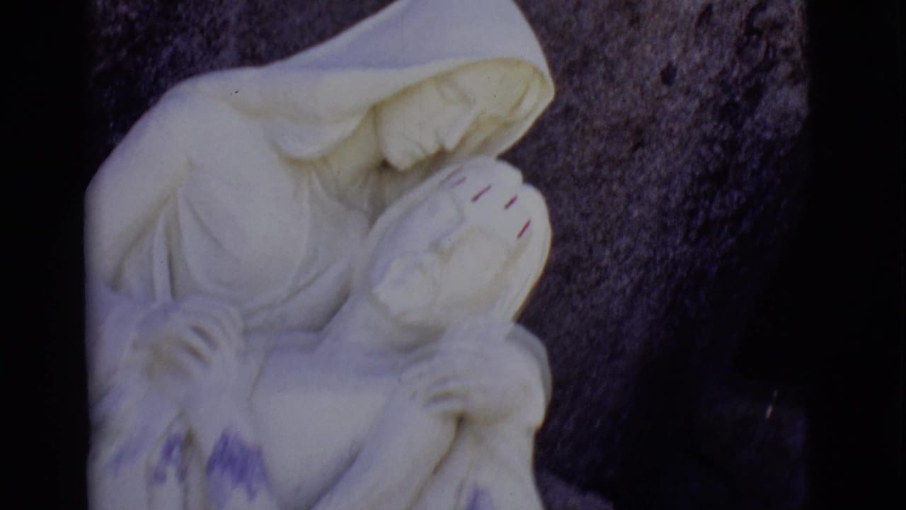 White Pieta-like statue against dark rocks with black film edges.