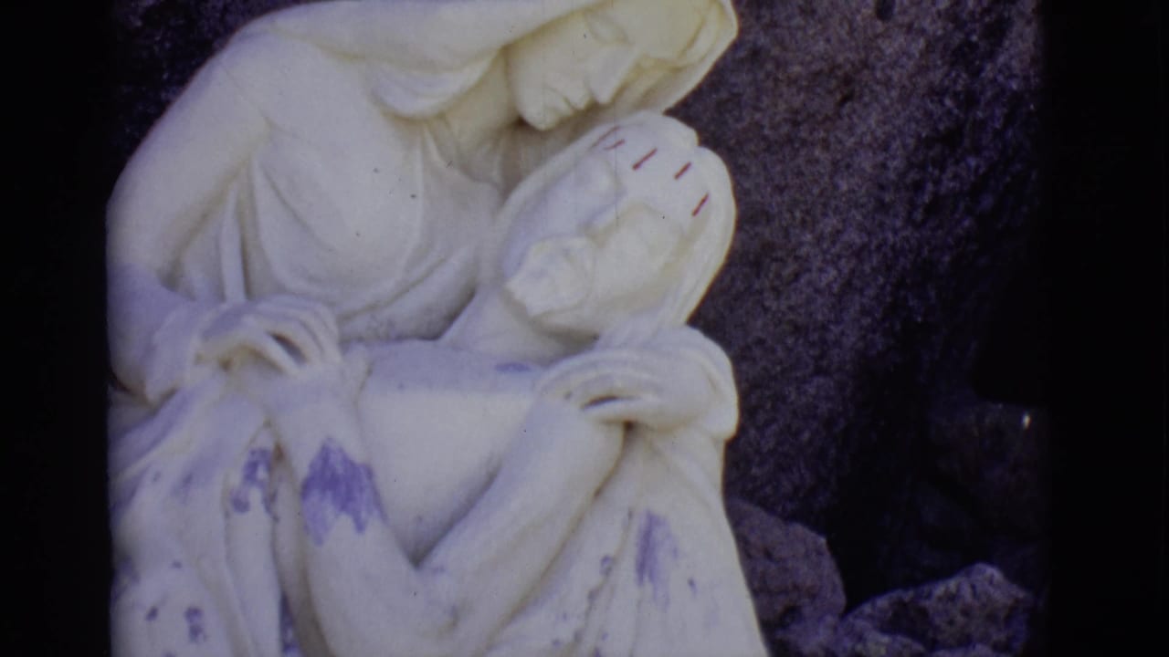 White devotional statue with cradled figure before a dark rock wall.