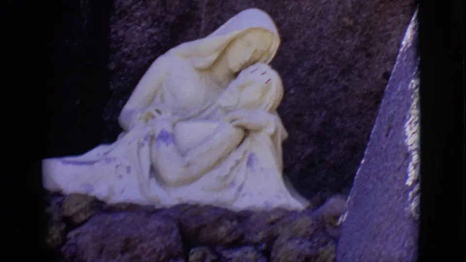 A wider 1965 San Luis, Colorado frame shows the full white Pieta-like statue seated among rocks before a dark backdrop.