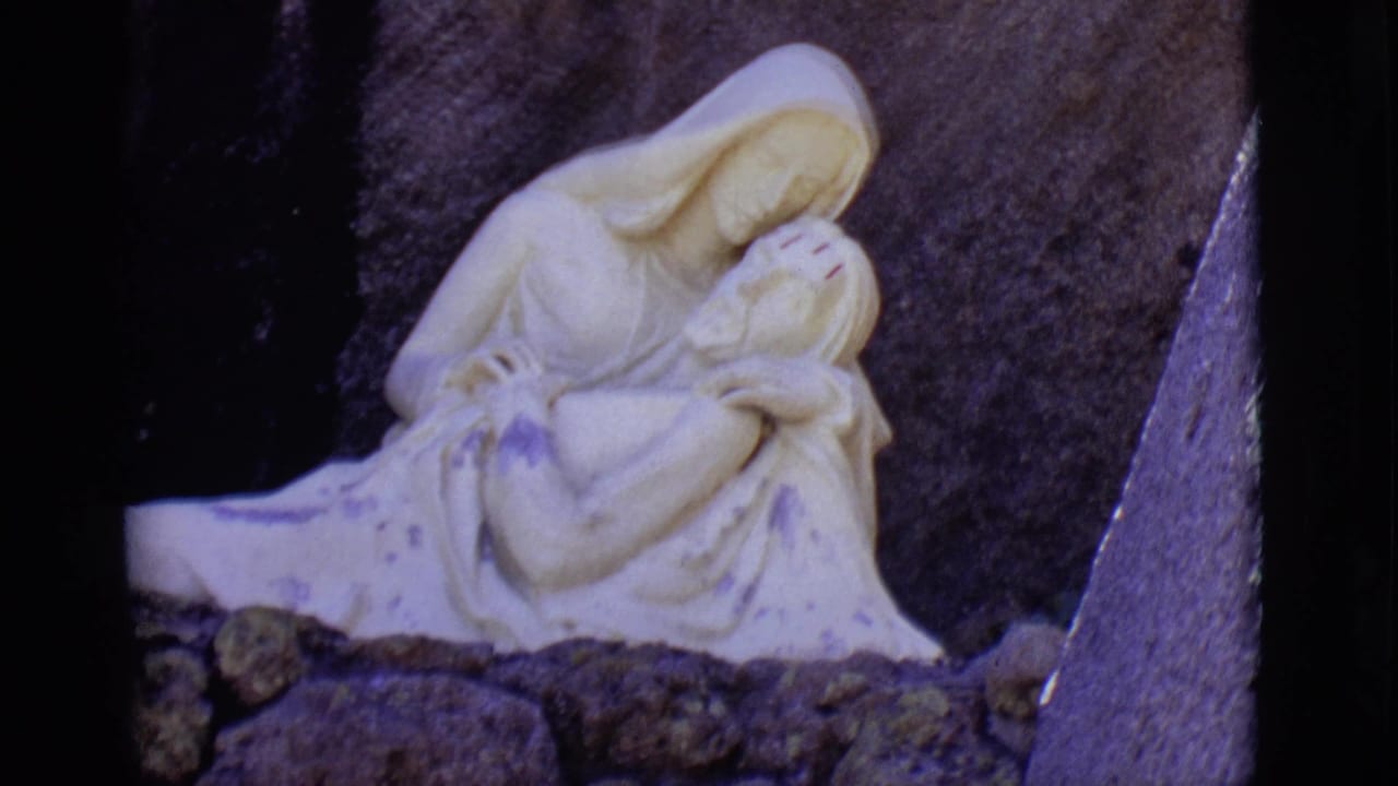White sculpture of Mary cradling Jesus against dark stone.