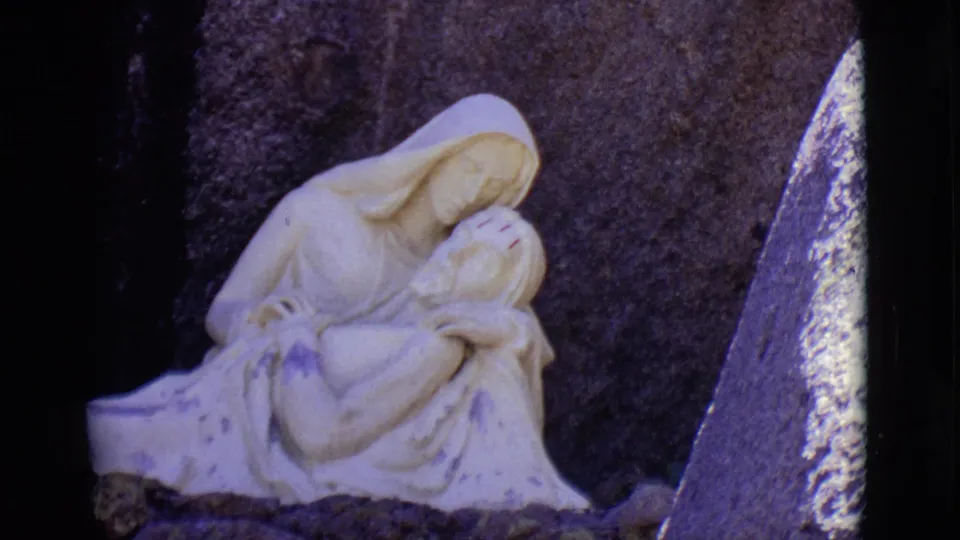 A closer 1965 home-movie view shows the white religious sculpture, visible staining, and rough stone setting in San Luis, Colorado.