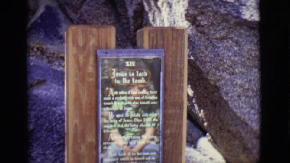A wooden sign identifies the 14th Station, 'Jesus is laid in the tomb,' within the San Luis, Colorado religious display.