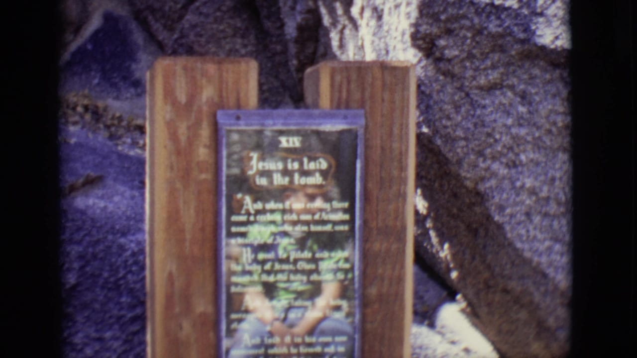 Wooden sign for Station XIV, Jesus is laid in the tomb, against a stone wall.