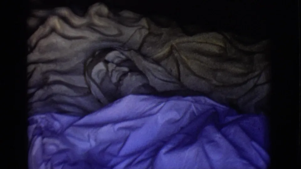 Dim 1965 8mm frame of a tomb tableau, with a sculptural figure lying under purple and gray drapery.