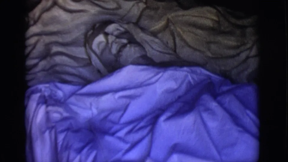 1965 San Luis, Colorado 8mm frame showing wrinkled blue plastic near a pale skull-like form in low light.