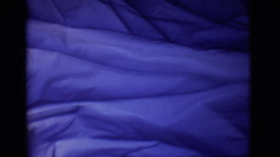 1965 San Luis, Colorado 8mm frame showing blue plastic spread across a dark, shadowed surface.