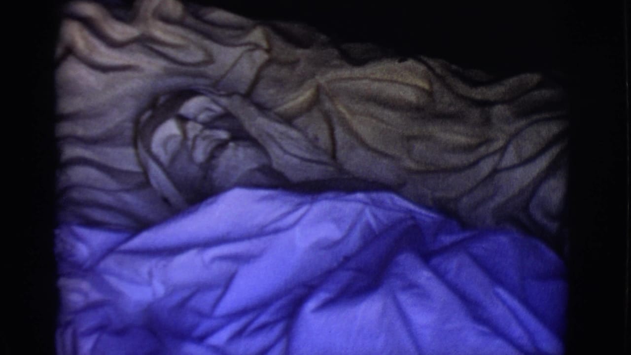 Reclining Jesus statue partly covered by a blue sheet and gray textile in dim light.