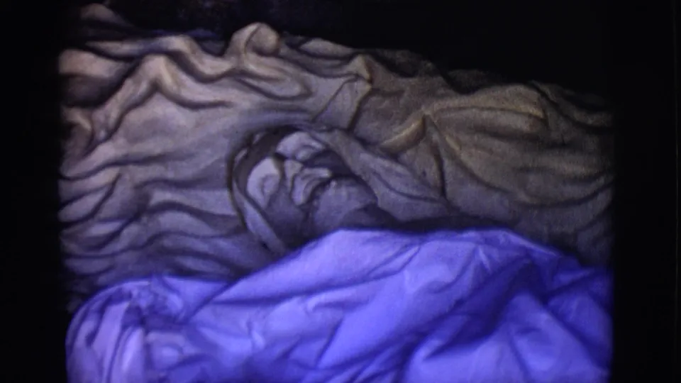 A slightly shifted 1965 8mm view shows the reclining Jesus statue under gray cloth and vivid blue fabric, with the face in shadow.