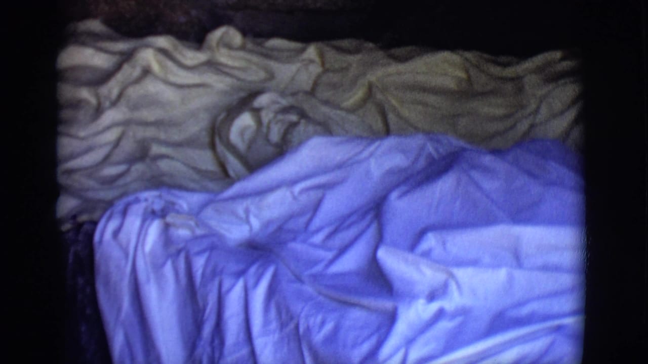 Rumpled blue and tan blankets against a dark background in a vintage film frame.