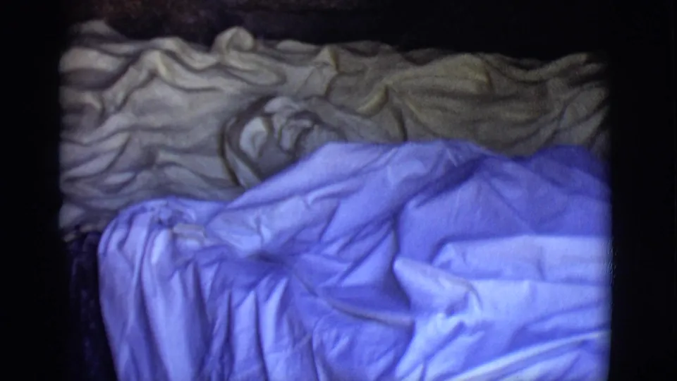 1965 San Luis, Colorado 8mm frame showing rumpled blue and tan blankets in a dim close-up with dark film edges.
