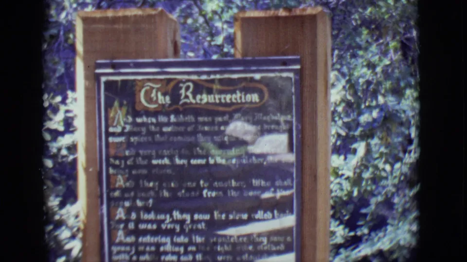 1965 San Luis, Colorado frame showing a brown wooden sign headed The Resurrection, filmed outdoors in bright foliage.