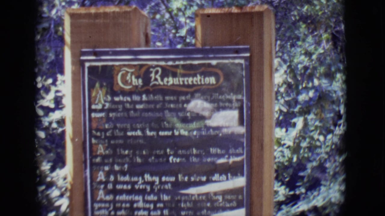 Wooden sign titled The Resurrection set outdoors among trees.