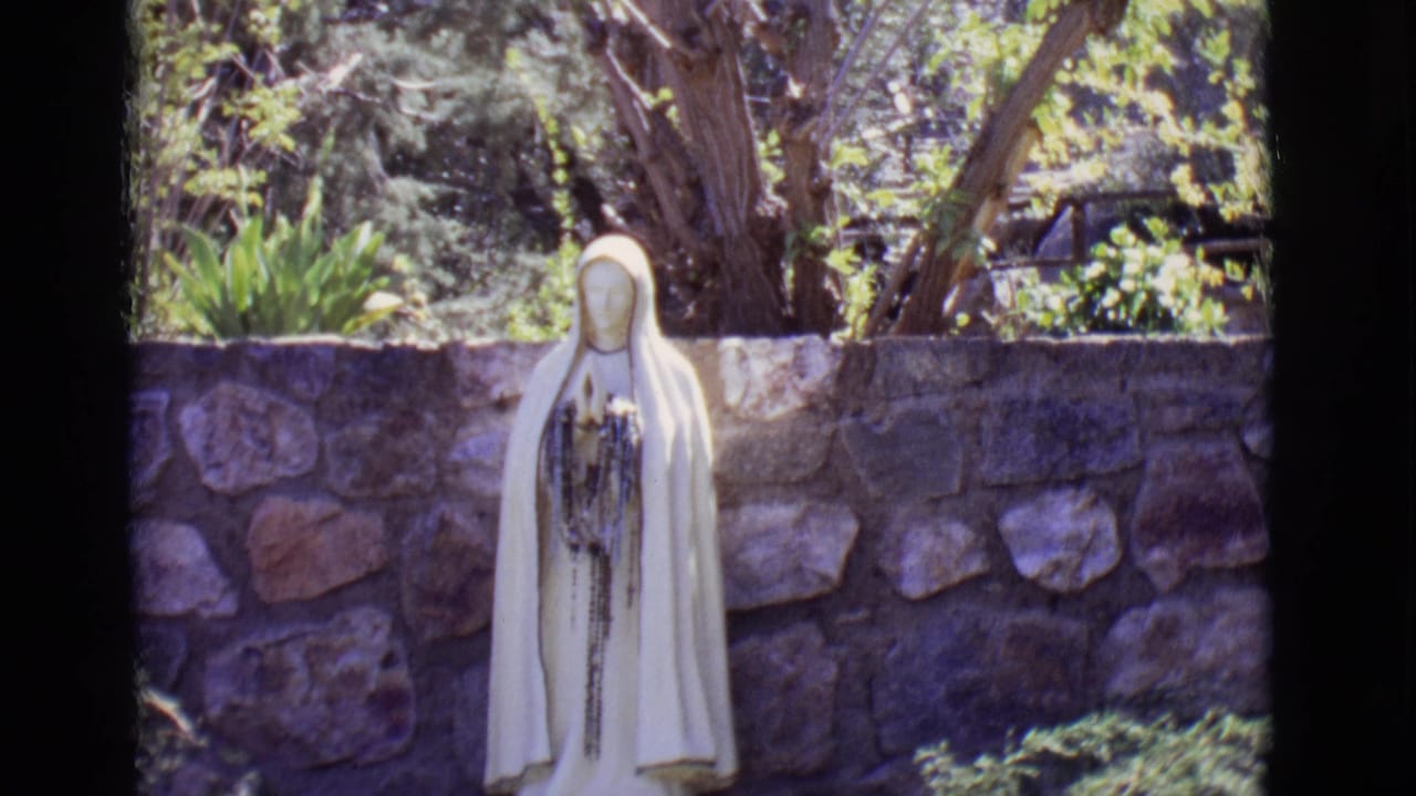 Mary statue in a garden setting with stone wall and trees behind it.