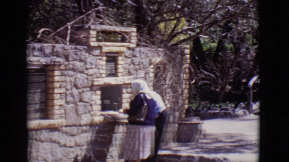 A woman in a headscarf and long skirt appears at a stone chapel or shrine structure in the 1965 San Luis, Colorado footage.