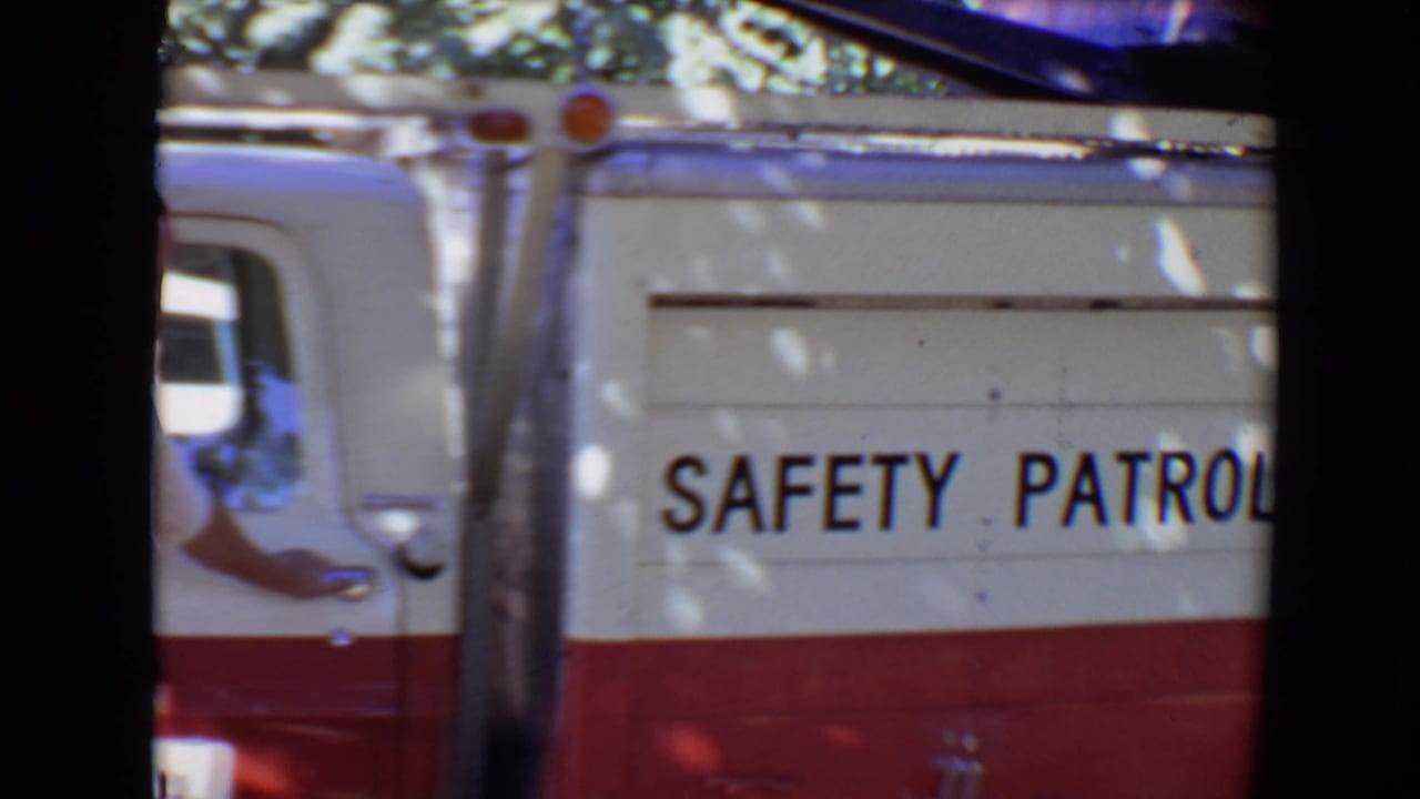 Red-and-white safety patrol truck partly seen through dark film-frame borders.