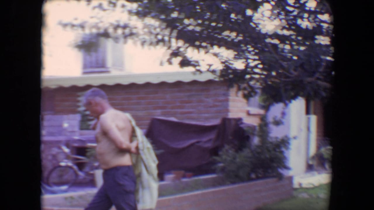Man walks beside a brick house with a striped shirt over one shoulder.