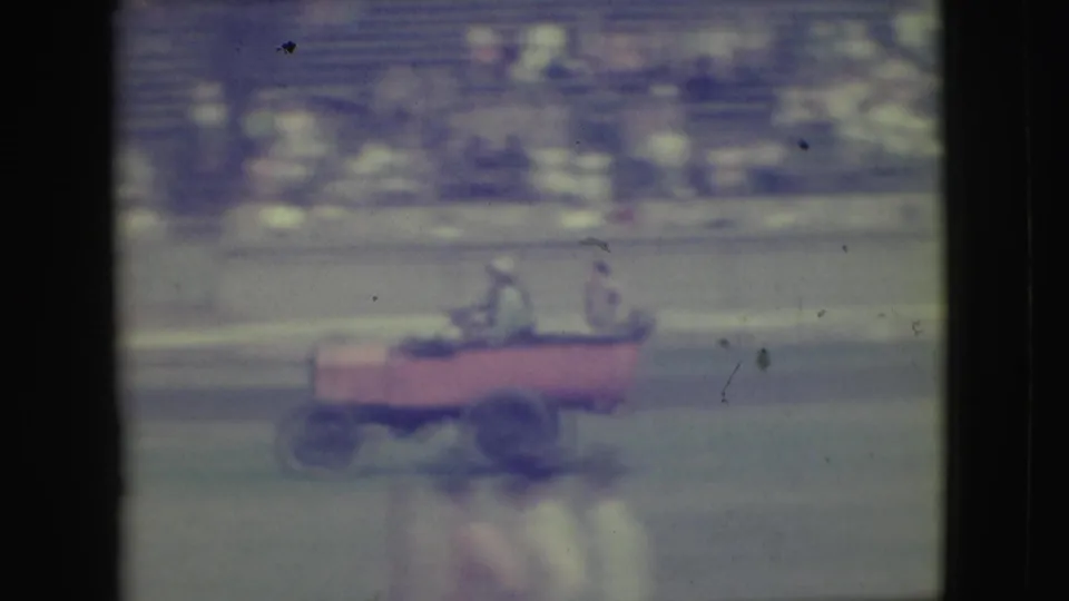 A red open vehicle with seated passengers crosses the track area in the 1949 Denver home-movie sequence.