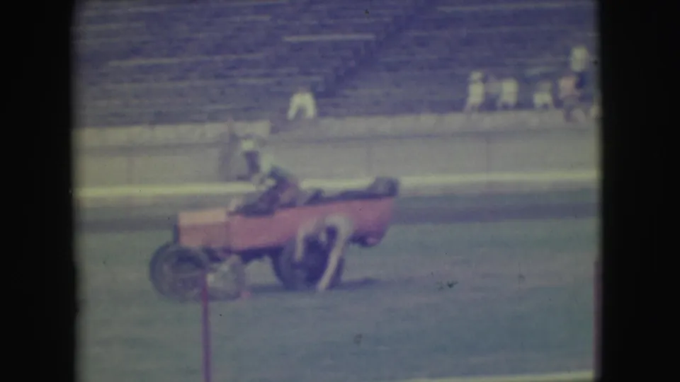 Near the end of the Denver home-movie clip, one adult rider appears partly outside the small pink car as the vehicle sits or moves on the grassy field.