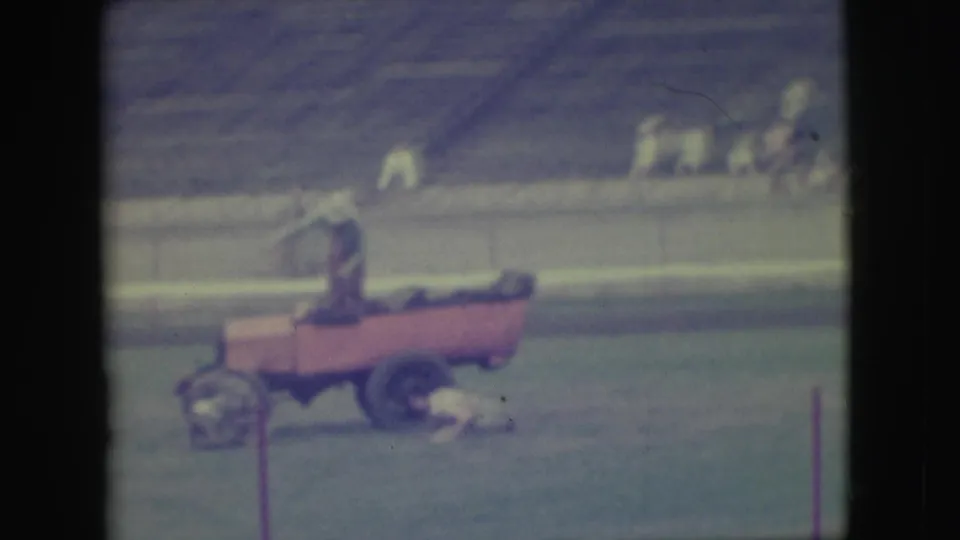 1949 Denver home-movie frame showing a person on a red field cart while another figure stands on the grass near empty bleachers.