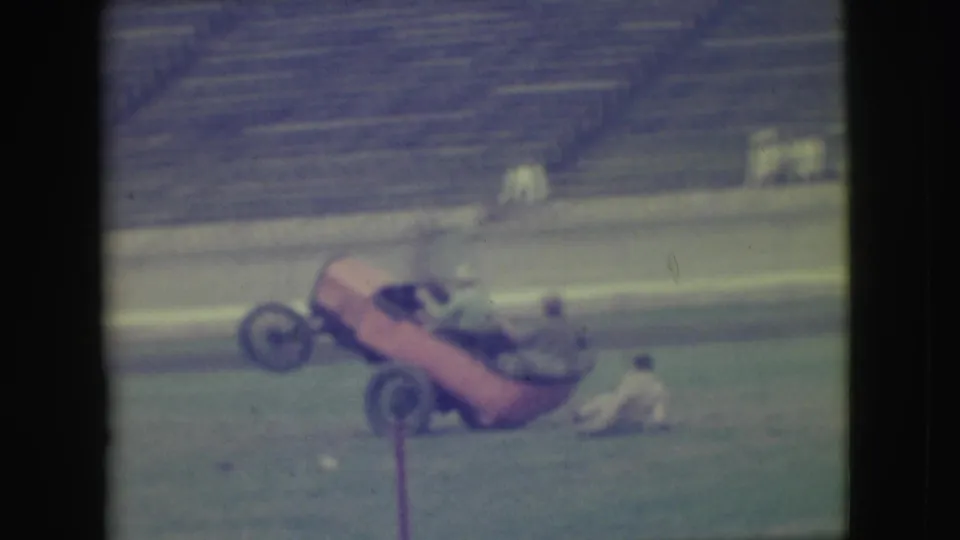 The Denver stadium stunt ends with the red open car tilted upward and a person appearing to fall or sit on the field nearby.
