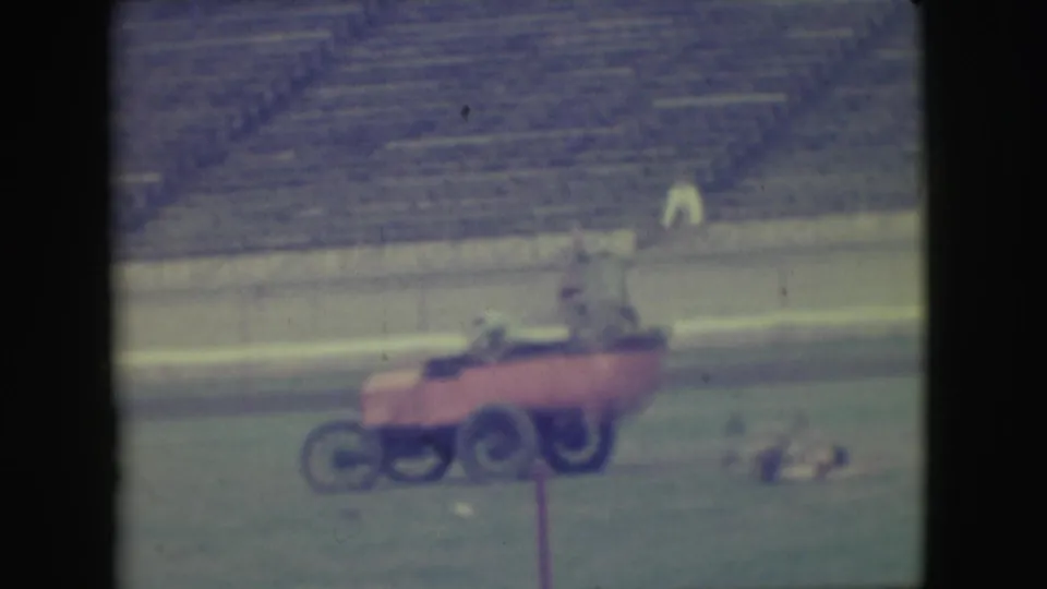 In 1949 Denver home-movie footage, three men appear to ride a red cart across a grassy field with empty bleachers behind them.