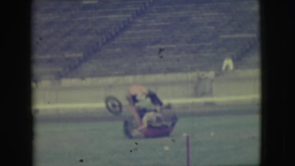 The cart appears to roll or tip on the stadium grass, with a wheel raised and riders partly obscured by motion blur.