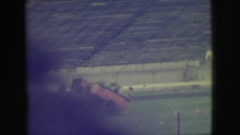 At the end of the 1949 Denver clip, the red cart lies tipped on the grass near blurred adult figures and stadium bleachers.