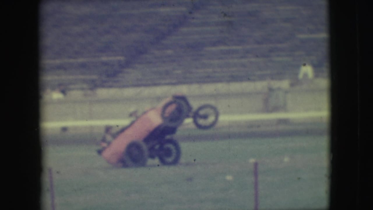Red experimental vehicle tilted upward with front wheels raised on a grassy field.
