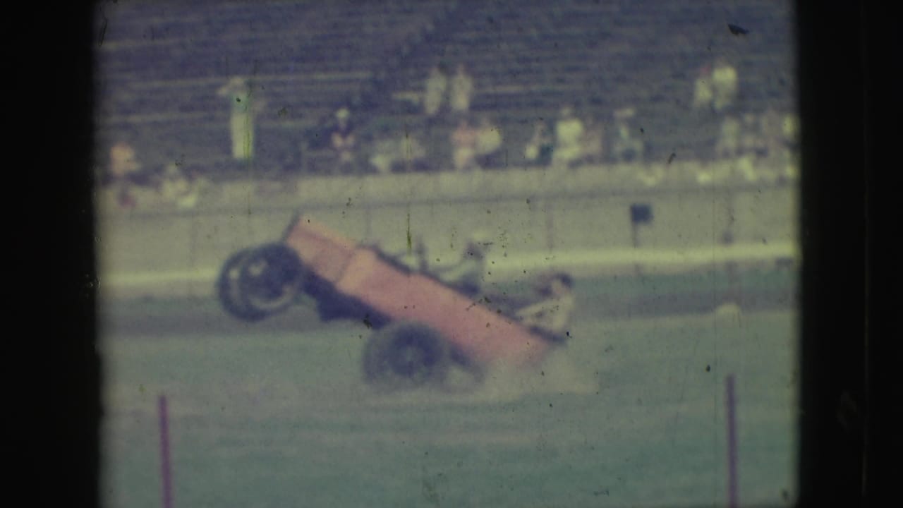1949 Denver frame showing the orange stunt car at a steep angle during a two-wheel driving maneuver on grass.