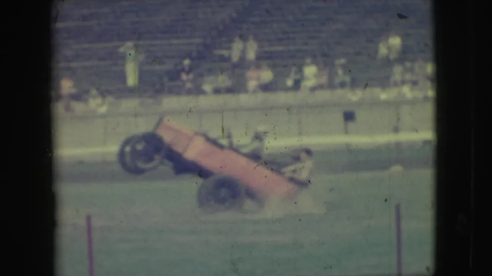 1949 Denver frame showing the orange stunt car at a steep angle during a two-wheel driving maneuver on grass.