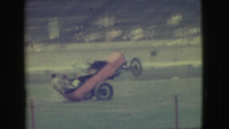 1949 Denver home-movie frame of the stunt car reaching a near-vertical angle while performing for a seated crowd.