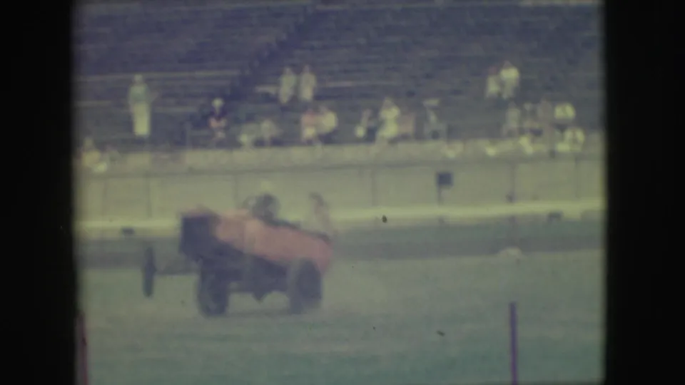 1949 Denver frame showing the orange stunt car leveling out after a two-wheel maneuver in front of bleachers.