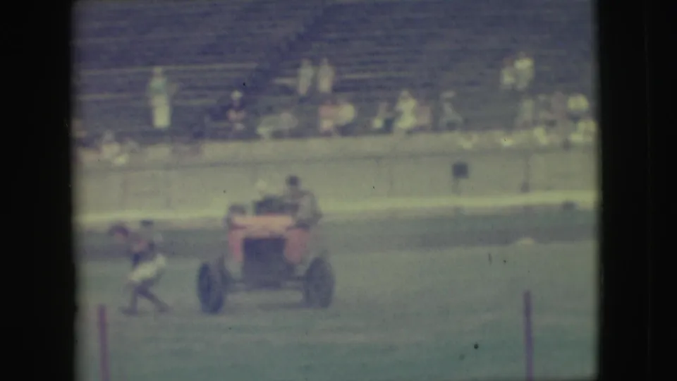1949 Denver home-movie frame showing a small rider on a red motorized vehicle, with bleachers and spectators in the background.