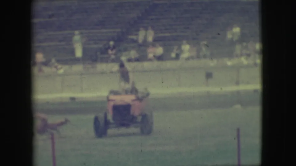 1949 Denver frame of a red motorized ride on a grassy fairground, with the rider upright and spectators seated behind.