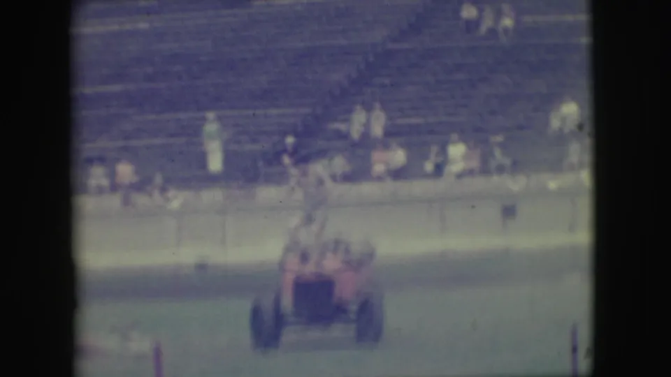 Soft 8mm frame from 1949 Denver showing a small red motorized vehicle on grass before bleachers and spectators.