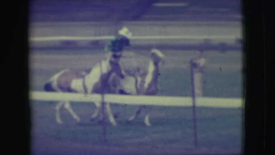 A rider in dark clothing stands over two trained horses trotting together in the 1949 Denver arena footage.