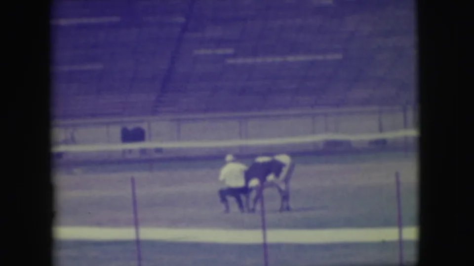 In supplied 1949 Denver rodeo footage, adult participants appear near a bull or steer in a dirt arena with empty bleachers behind them.