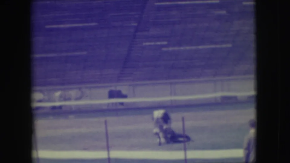 The 1949 rodeo action shows a participant down near the animal on the dirt, filmed from the stands through soft, color-shifted 8mm footage.