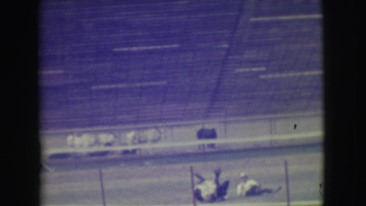 Racetrack scene with riders and a horse near the rail after a fall.