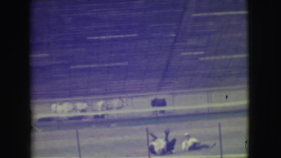 A Denver horse race moment shows riders and horses clustered near the rail after an apparent fall, with bleachers behind them.