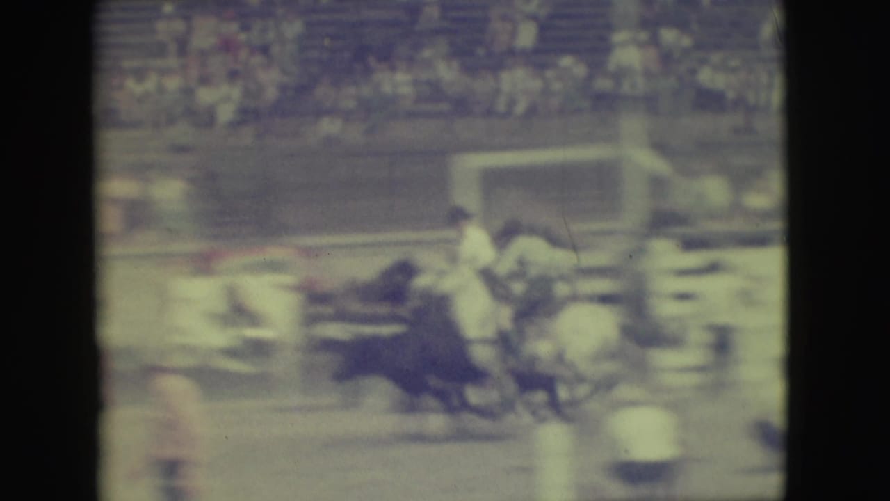 1949 Denver rodeo footage showing a mounted rider near a dark bull in front of blurred arena bleachers.