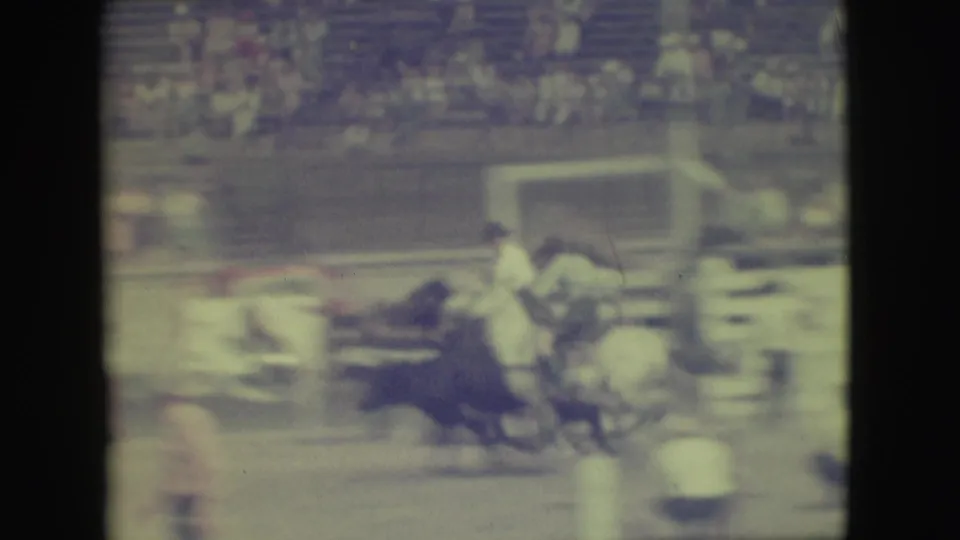 1949 Denver rodeo footage showing a mounted rider near a dark bull in front of blurred arena bleachers.