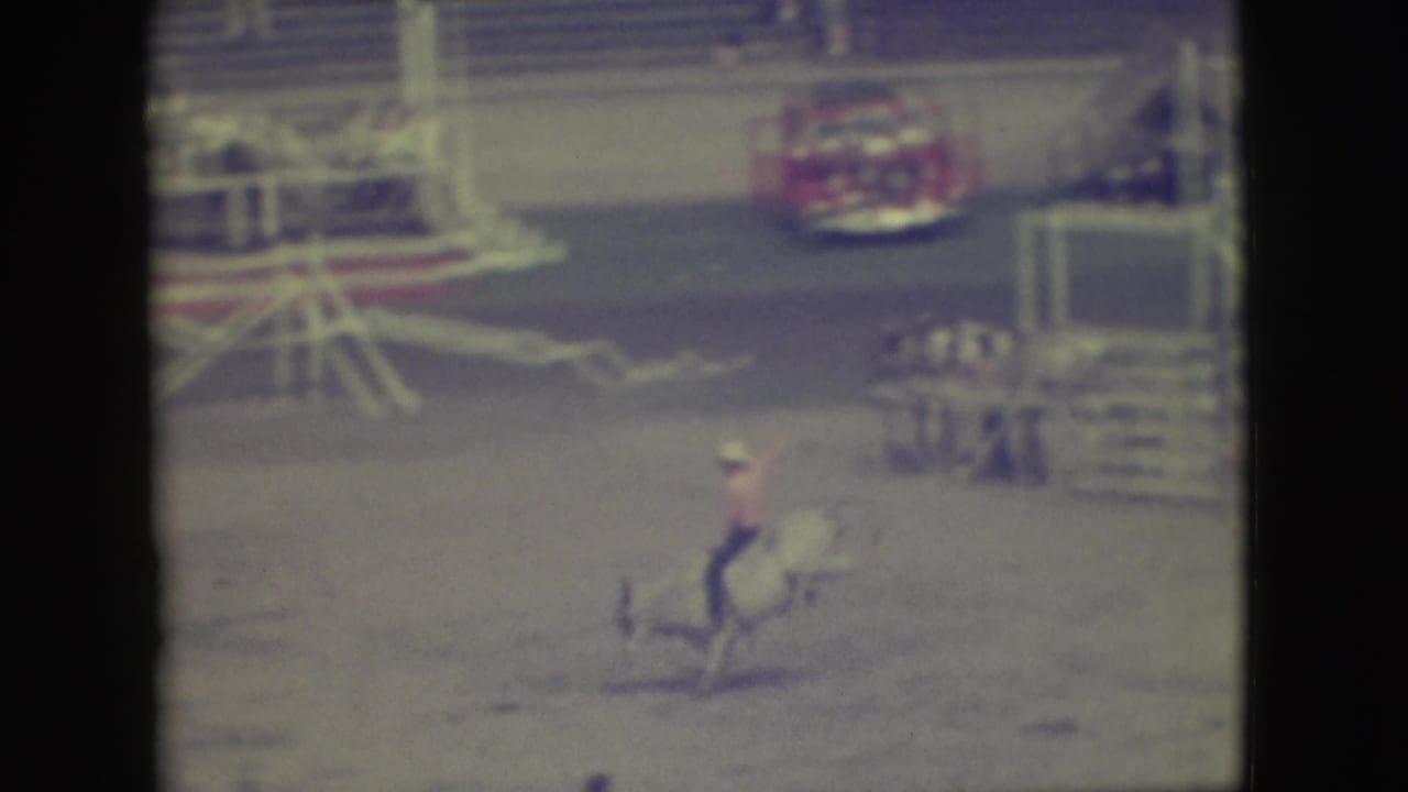 Rider in a light hat on a bucking bull in a dusty rodeo arena.
