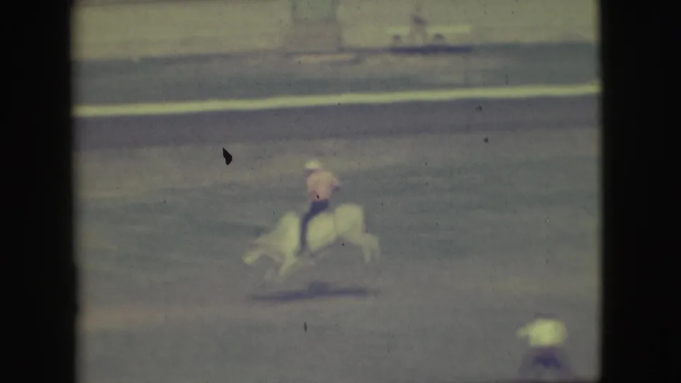 A distant 1949 Denver rodeo frame shows the rider leaning hard while the bull bucks, with faded color and dark 8mm edges.