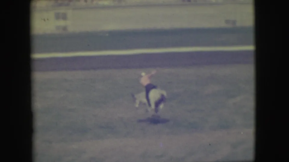 In the Denver 1949 rodeo footage, a cowboy in a light shirt rides a white bull as it bucks across the arena.