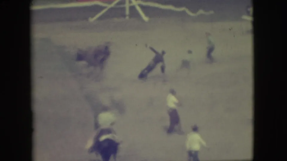 1949 Denver rodeo frame showing a rider falling or on the ground near a brown bull, with several people positioned around the arena.