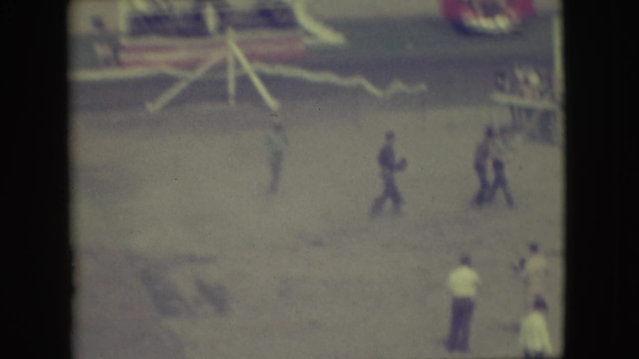 Men move across a dusty arena near railings and bunting.