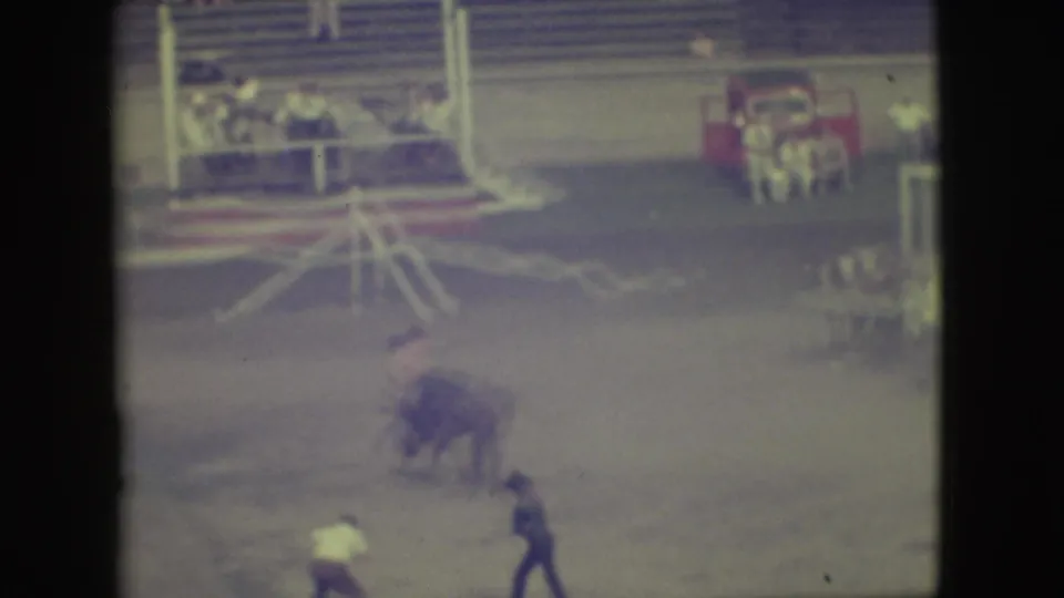 1949 Denver frame showing a bull moving through dust in the arena with a man positioned nearby and bunting behind.